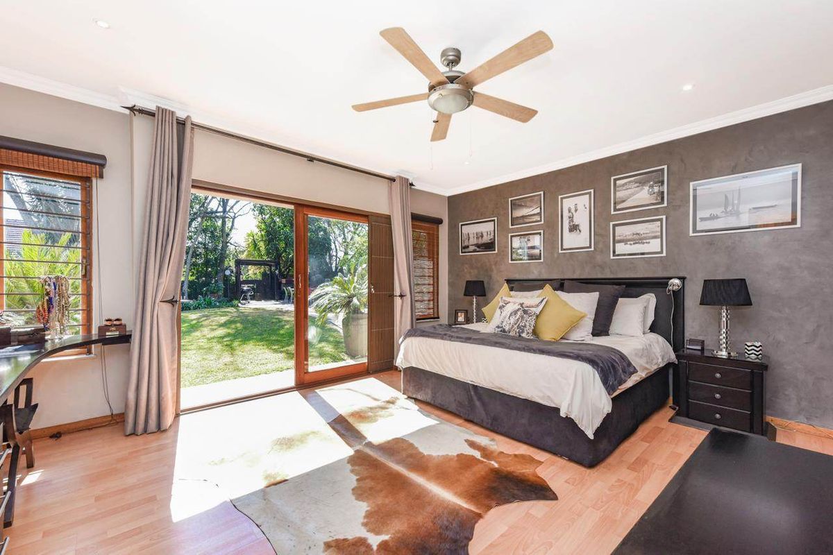 Spacious bedroom featuring a textured accent wall, ceiling fan, and large sliding glass doors providing direct access to the rear garden.