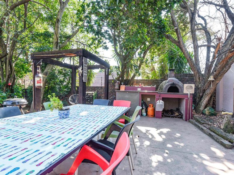Outdoor patio area featuring a built-in pizza oven, concrete flooring, and a timber pergola, set within a mature garden environment.