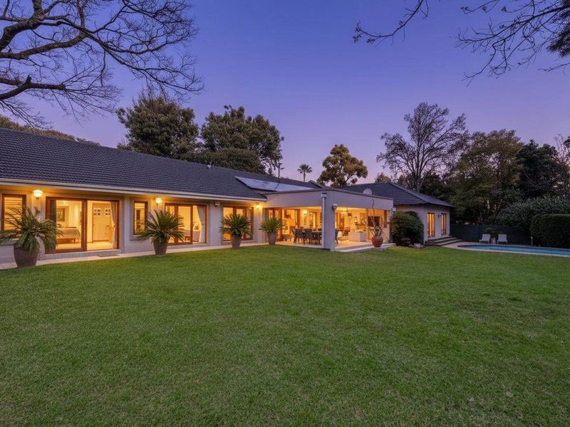 Spacious rear exterior view featuring a well-maintained lawn, covered patio area, swimming pool, and large sliding glass doors leading into the home.