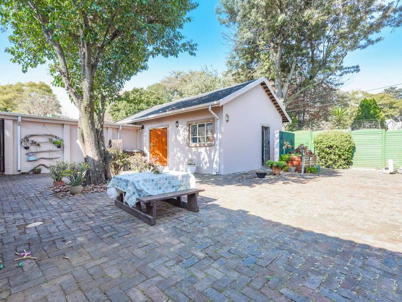 A spacious rear courtyard featuring paved flooring, mature trees, and access to a detached outbuilding with a tiled roof.