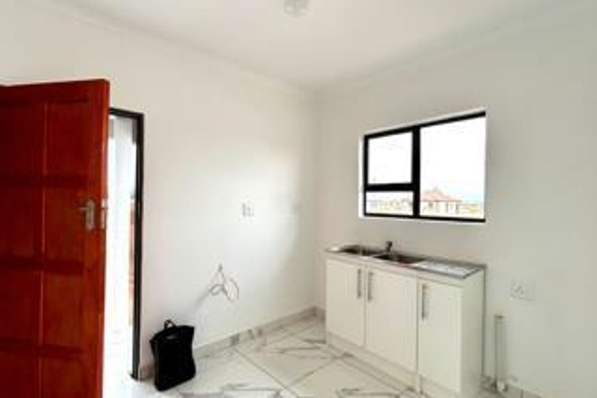 A clean, empty kitchen area featuring tiled flooring, built-in base cabinetry with a stainless steel sink, and a large window.