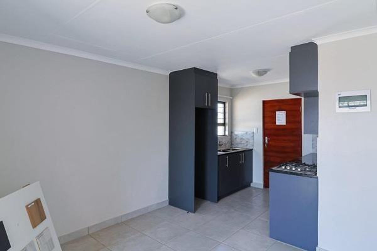 A clean, modern kitchen featuring dark grey cabinetry, a gas hob, double sink, and neutral tiled flooring in an open-plan layout.
