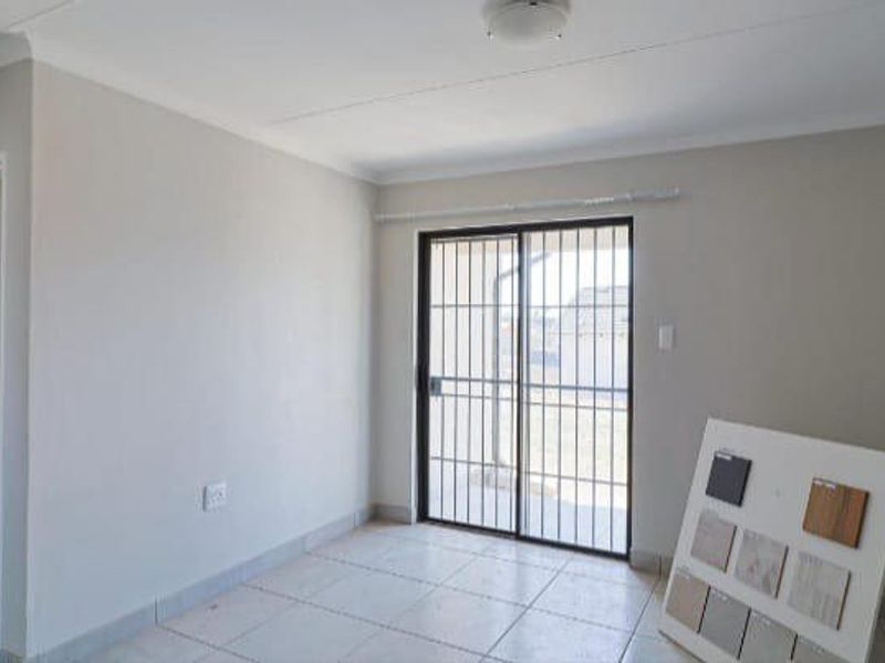A bright, empty living area featuring neutral walls, tiled flooring, and a sliding glass door with a security gate leading to the exterior.
