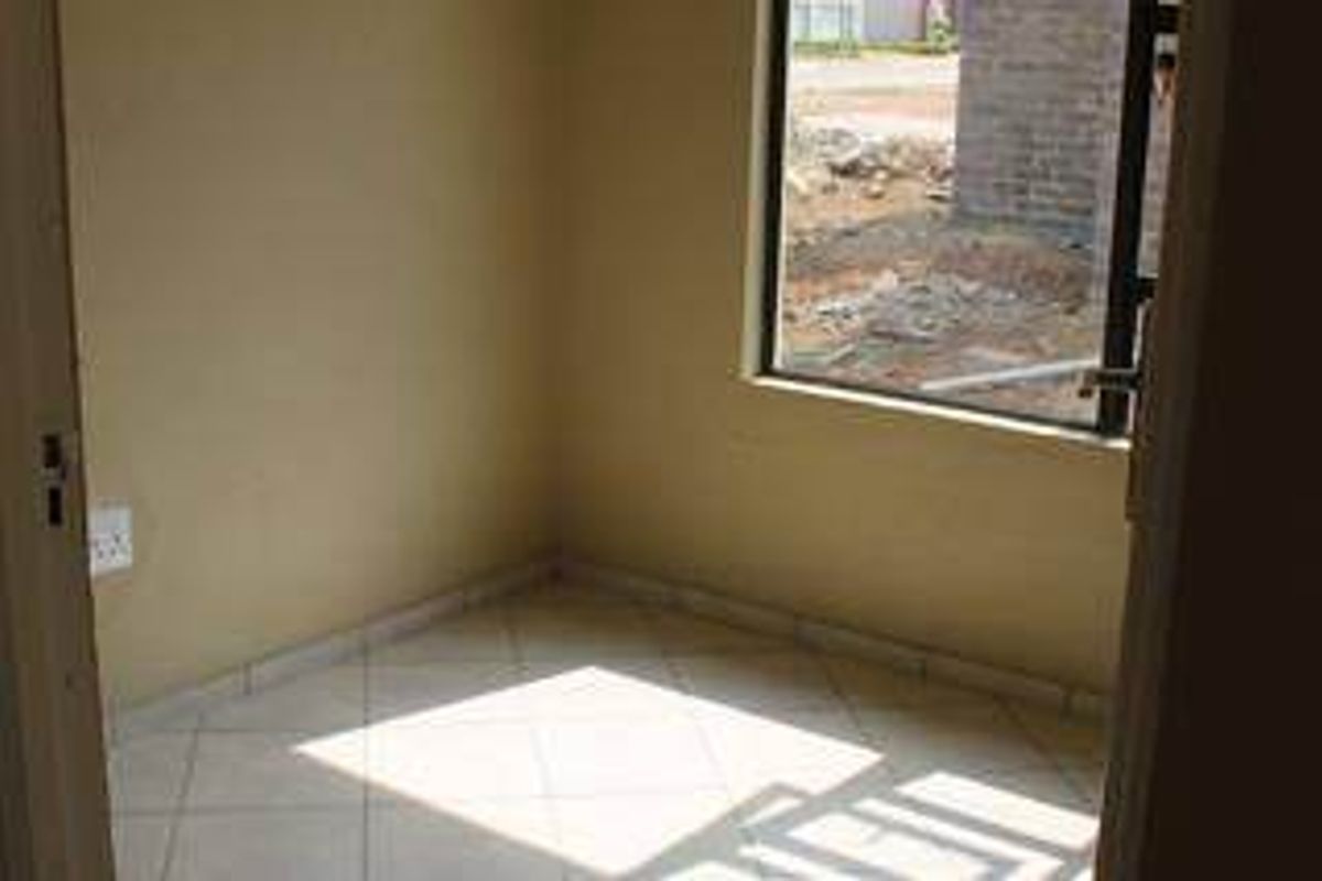 A compact, empty bedroom featuring tiled flooring and a large window, providing a blank canvas for interior design.