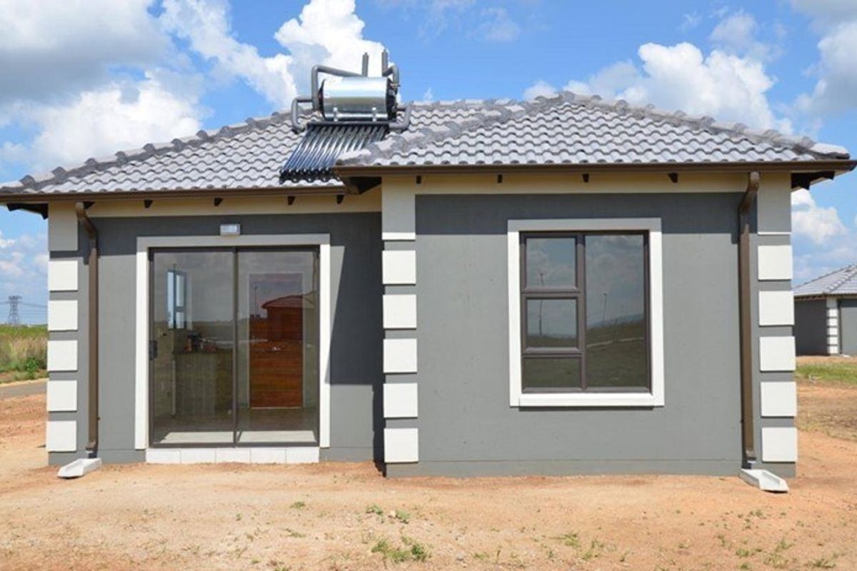 Rear view of a modern single-story house featuring a tiled roof, solar water heating system, sliding glass door, and grey exterior walls with white trim.