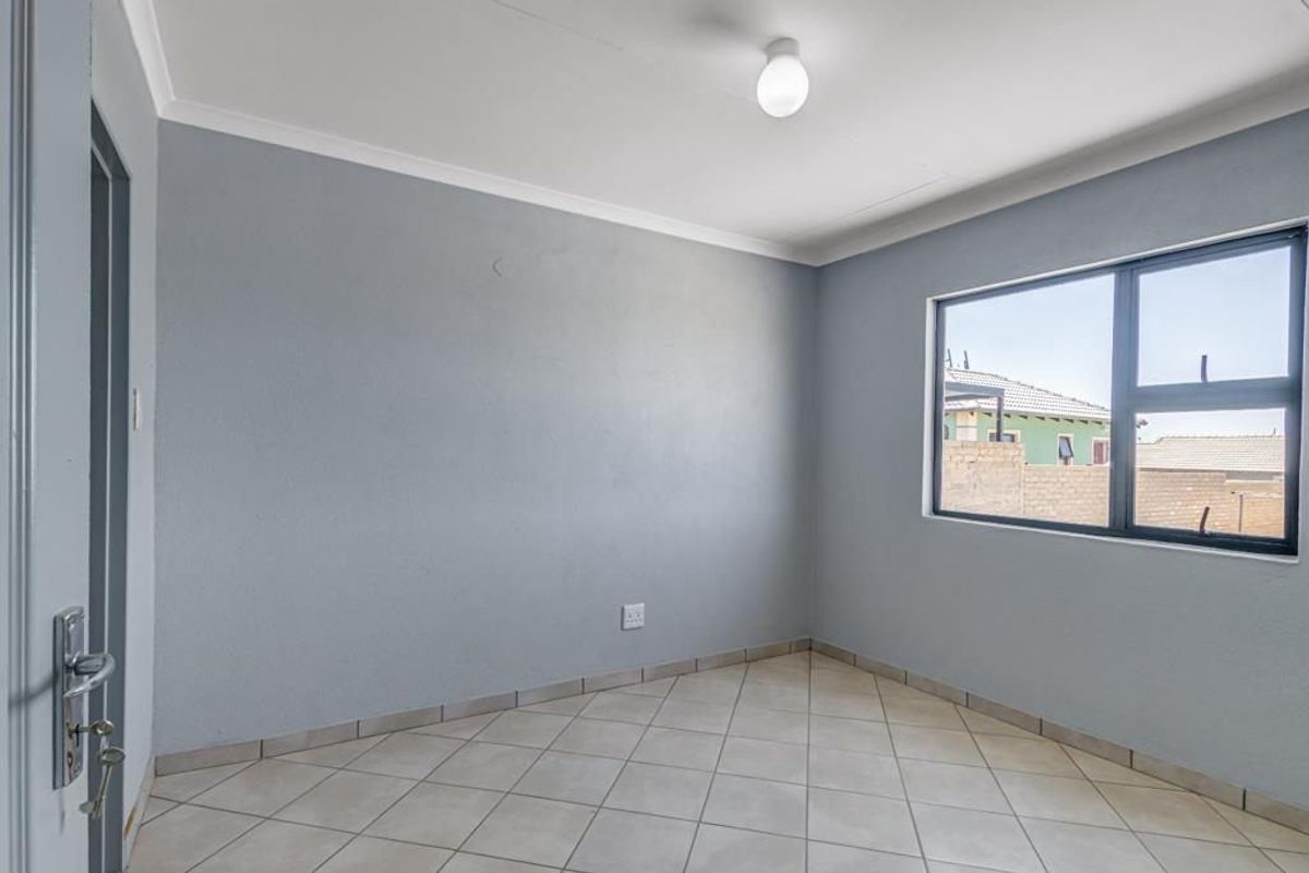 A clean, empty bedroom featuring neutral grey walls, tiled flooring, and an aluminium-framed window, providing a versatile space ready for personalization.