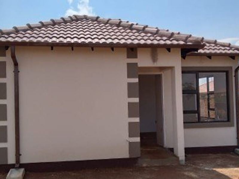 A view of the rear exterior of a modern single-story house featuring a tiled roof, aluminium window frames, and surrounding brick boundary walls.