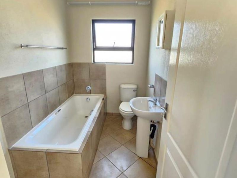 A functional bathroom featuring a bathtub with tiled surround, pedestal basin, and toilet, finished with neutral wall paint and tiled flooring.