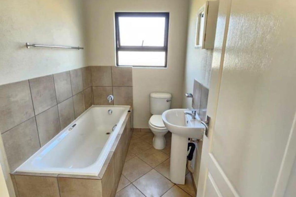 A functional bathroom featuring a bathtub with tiled surround, pedestal basin, and toilet, finished with neutral wall paint and tiled flooring.