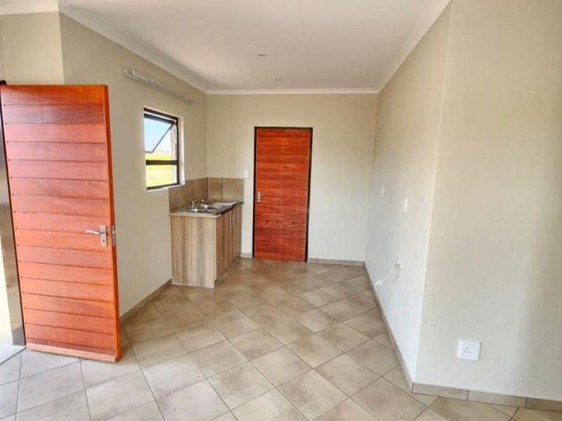 A compact, empty kitchen area featuring tiled flooring, wooden doors, and a small sink unit with built-in cabinetry.