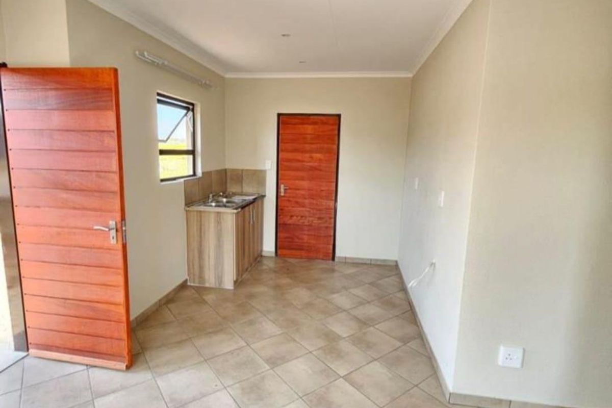A compact, empty kitchen area featuring tiled flooring, wooden doors, and a small sink unit with built-in cabinetry.