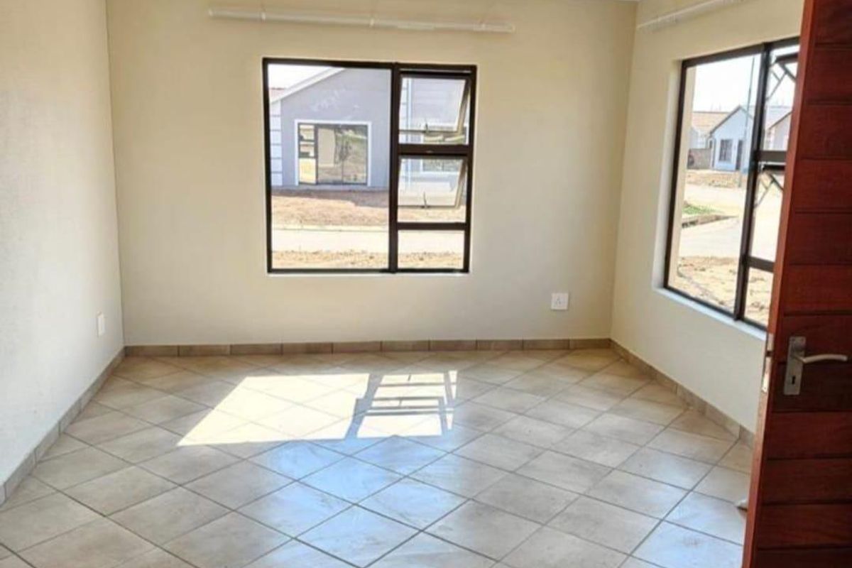 A bright, empty living area featuring neutral walls, tiled flooring, and large aluminium-framed windows providing natural light.