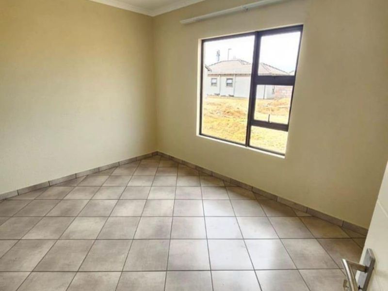 A clean, empty bedroom featuring neutral tiled flooring, a large aluminium-framed window, and a simple ceiling light fixture.