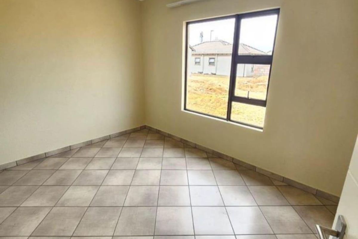 A clean, empty bedroom featuring neutral tiled flooring, a large aluminium-framed window, and a simple ceiling light fixture.