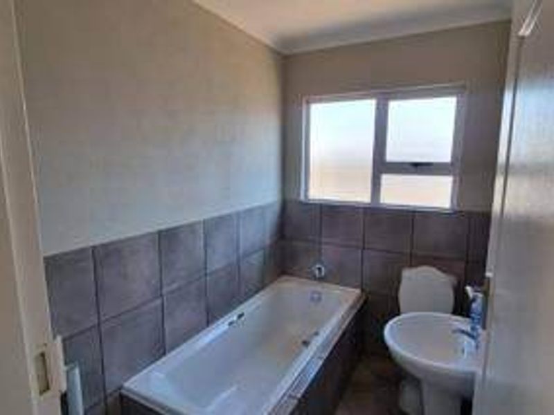 A functional bathroom featuring a built-in bathtub, pedestal basin, and toilet with neutral wall tiling and a frosted glass window for natural light.