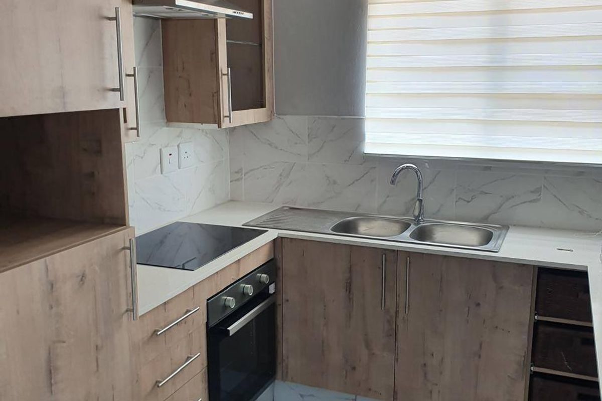 Modern kitchen featuring wood-look cabinetry, built-in oven and hob, stainless steel extractor, double sink, and marble-look tiled flooring and backsplash.