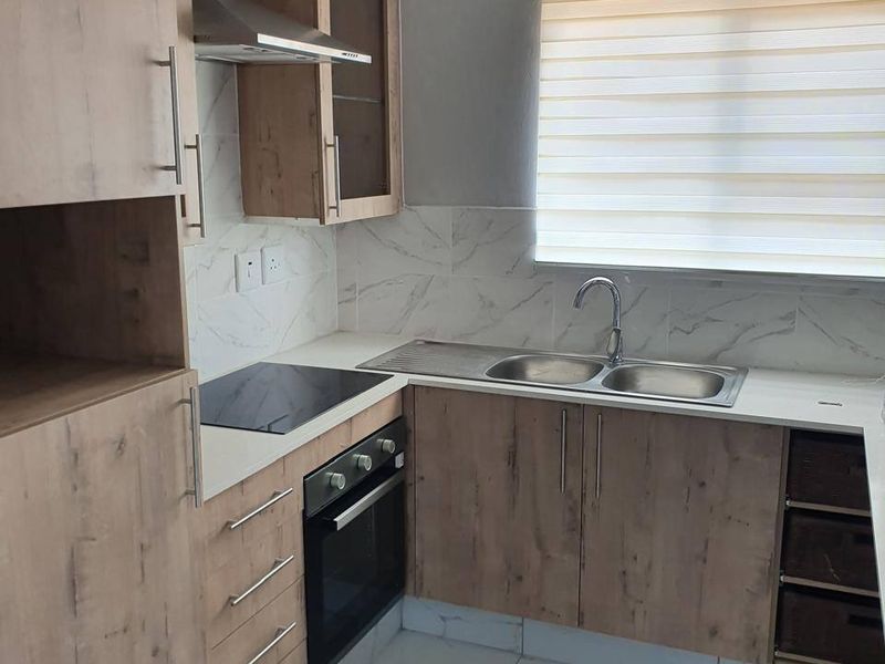 Modern kitchen featuring wood-look cabinetry, built-in oven and hob, stainless steel extractor, double sink, and marble-look tiled flooring and backsplash.