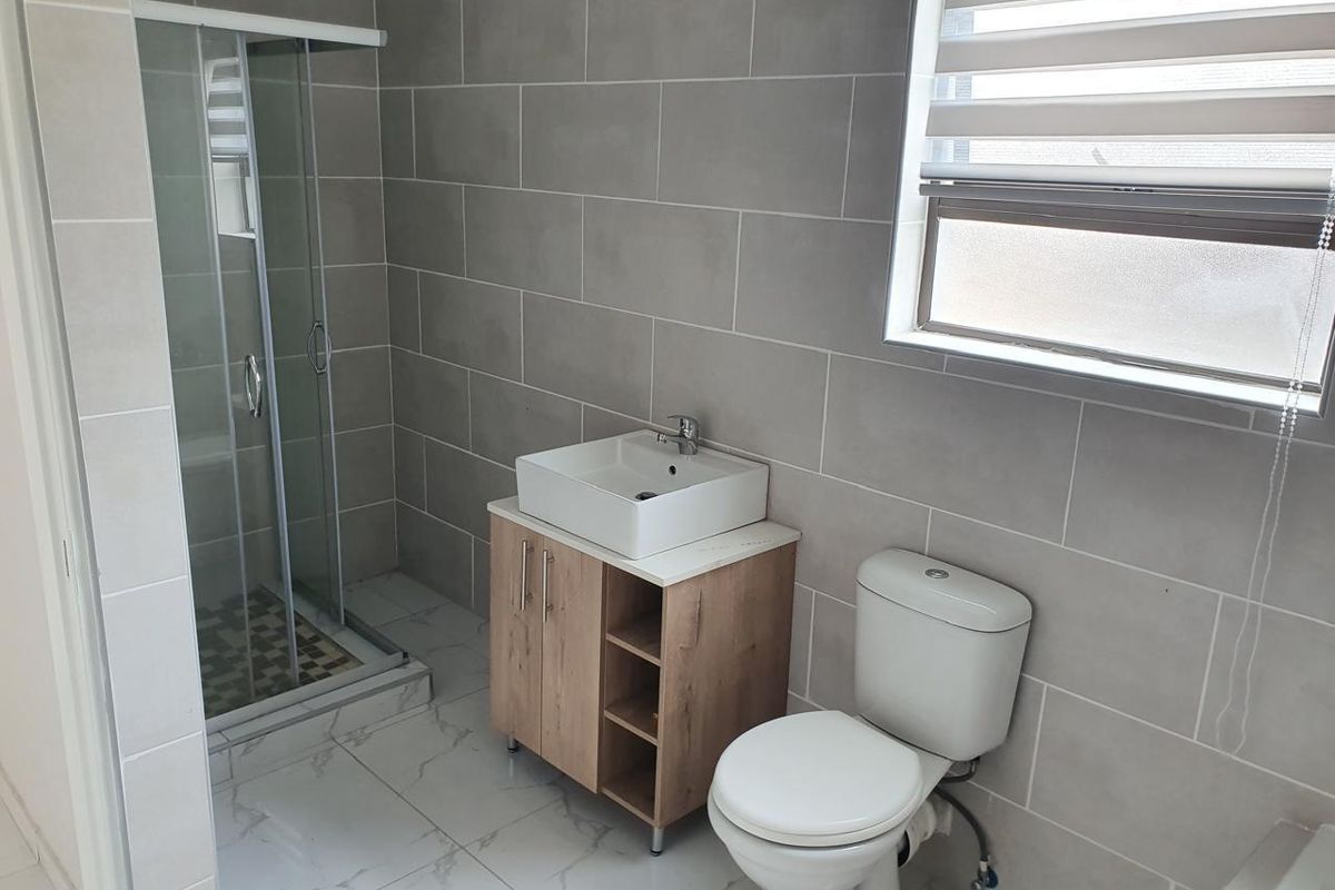 A modern, well-maintained bathroom featuring a glass shower enclosure, a contemporary vessel sink vanity, and neutral wall and floor tiling.