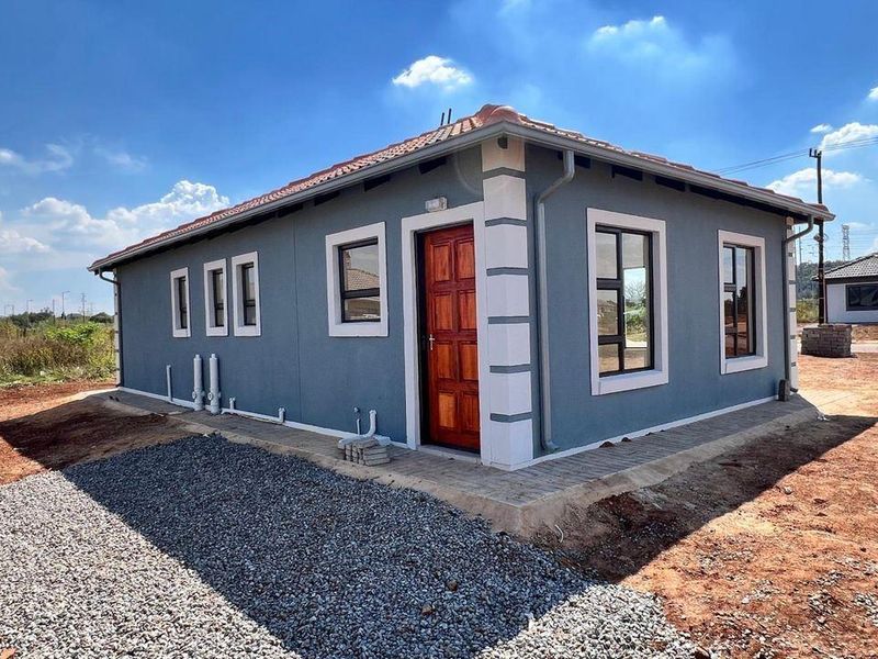 A view of the rear exterior of a modern house featuring plastered walls, a tiled roof, and paved walkways surrounding the structure.