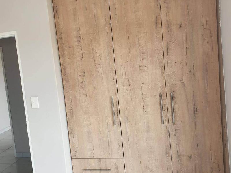 A bright bedroom featuring modern wood-look built-in wardrobes and clean, light-colored tiled flooring.