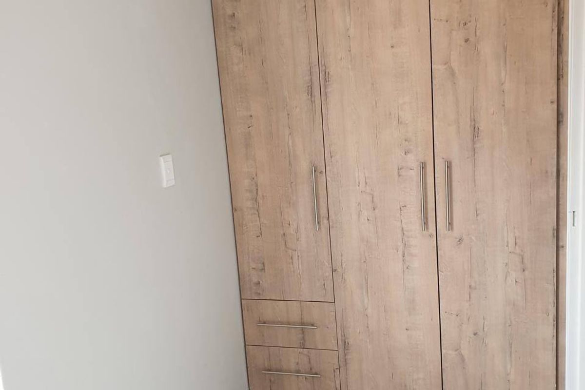 A clean, modern bedroom featuring light wood-grain built-in wardrobes and contemporary marble-look floor tiles.