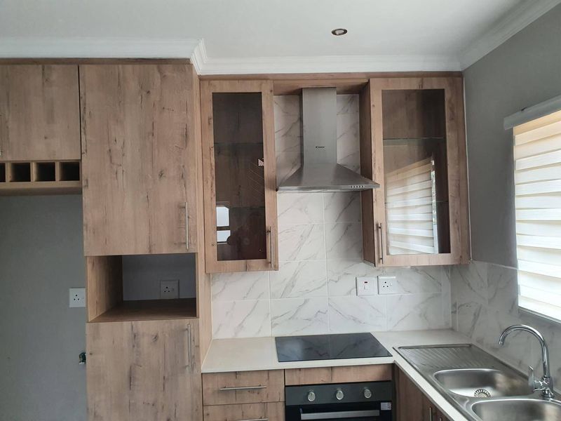 Modern kitchen featuring wood-look cabinetry, marble-style backsplash, integrated stainless steel appliances, and a double bowl sink with a contemporary mixer tap.