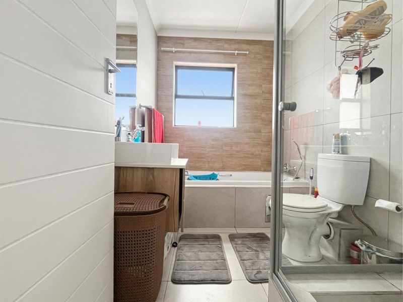A functional bathroom featuring a bathtub, separate shower enclosure, vanity basin, and toilet with neutral tiled finishes.