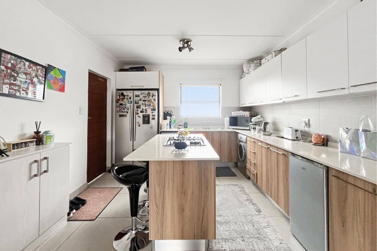 Modern kitchen featuring a central island with a gas hob, ample built-in cabinetry, stone countertops, and integrated laundry appliances.