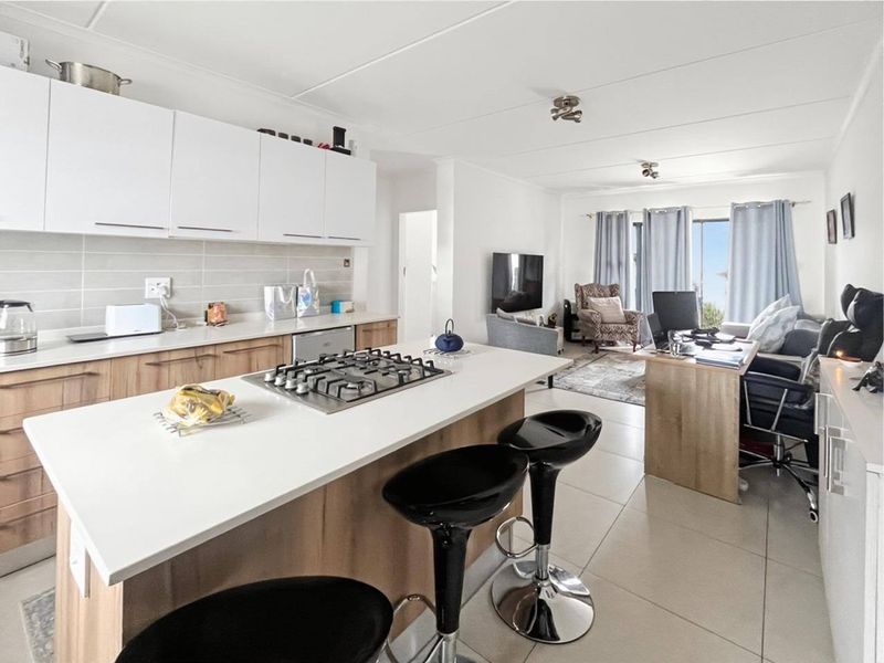 Modern open-plan living area featuring a contemporary kitchen with stone countertops, gas hob, and seamless flow to the lounge and balcony access.