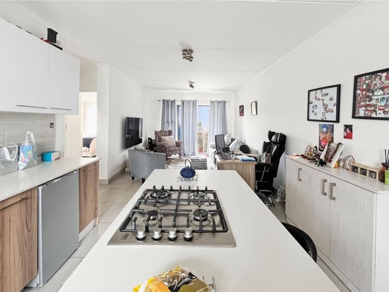Open-plan living area featuring a modern kitchen island with a gas hob, tiled flooring, and sliding doors leading to an outdoor space.
