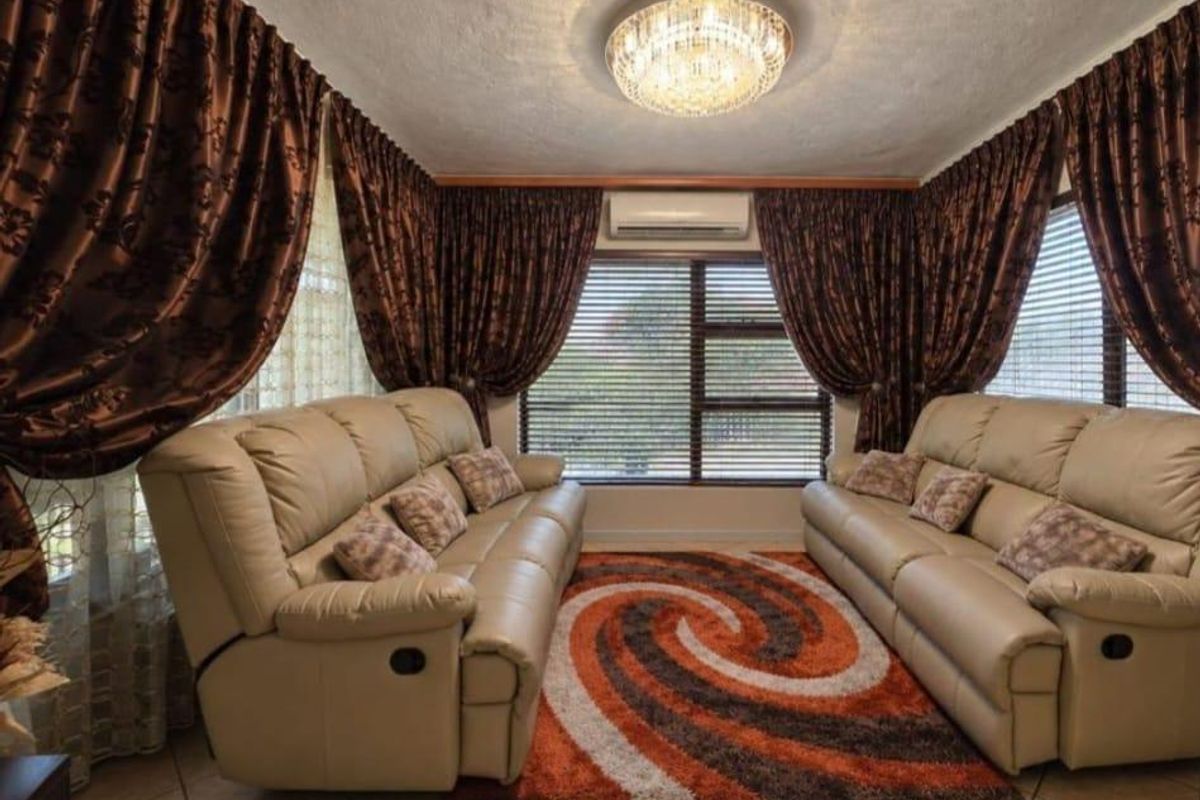 A comfortable living room featuring tiled flooring, a split-system air conditioner, and large windows with horizontal blinds, providing a bright and functional space.
