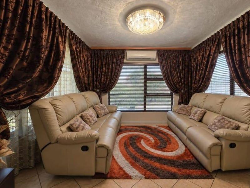 A comfortable living room featuring tiled flooring, a split-system air conditioner, and large windows with horizontal blinds, providing a bright and functional space.