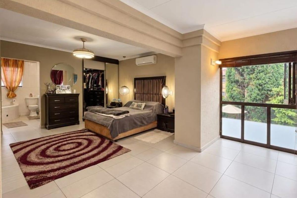 Spacious bedroom featuring tiled flooring, built-in cupboards, an integrated air conditioning unit, and an open-plan en-suite bathroom with sliding doors to the exterior.