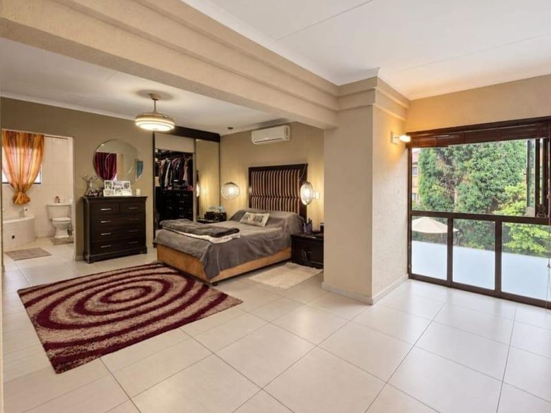 Spacious bedroom featuring tiled flooring, built-in cupboards, an integrated air conditioning unit, and an open-plan en-suite bathroom with sliding doors to the exterior.