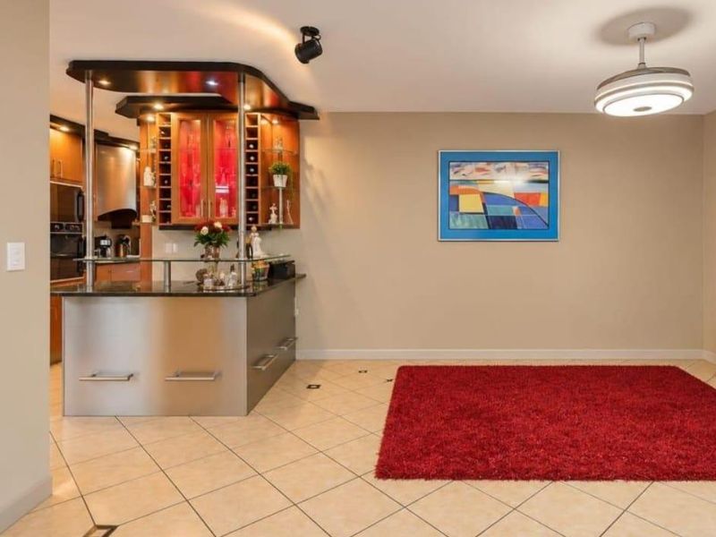 A well-maintained home bar area featuring a modern built-in counter with integrated cabinetry and stylish lighting, set against neutral walls and tiled flooring.
