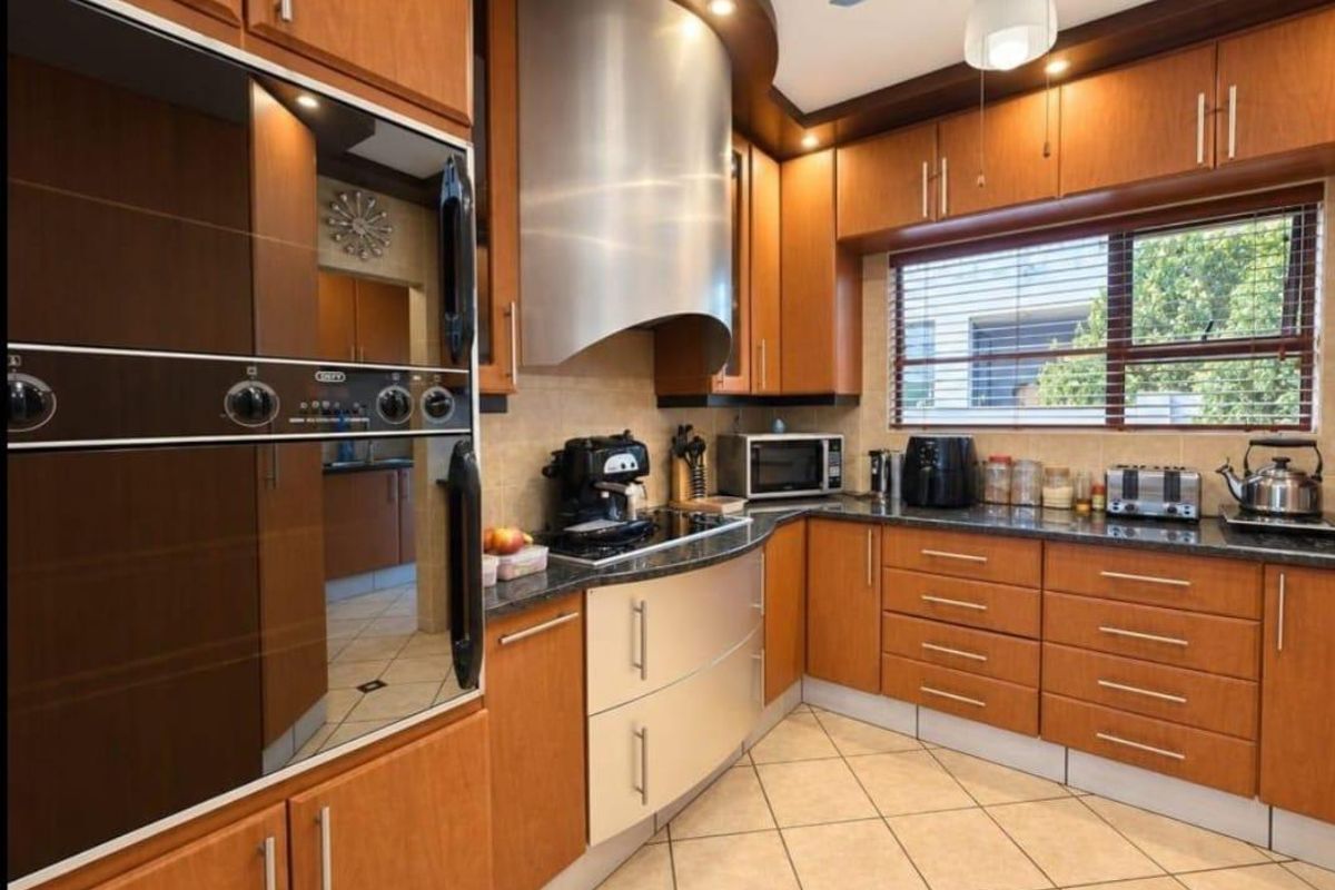 A well-maintained kitchen featuring warm wood cabinetry, granite countertops, a stainless steel extractor fan, and a built-in oven, complemented by tiled flooring.