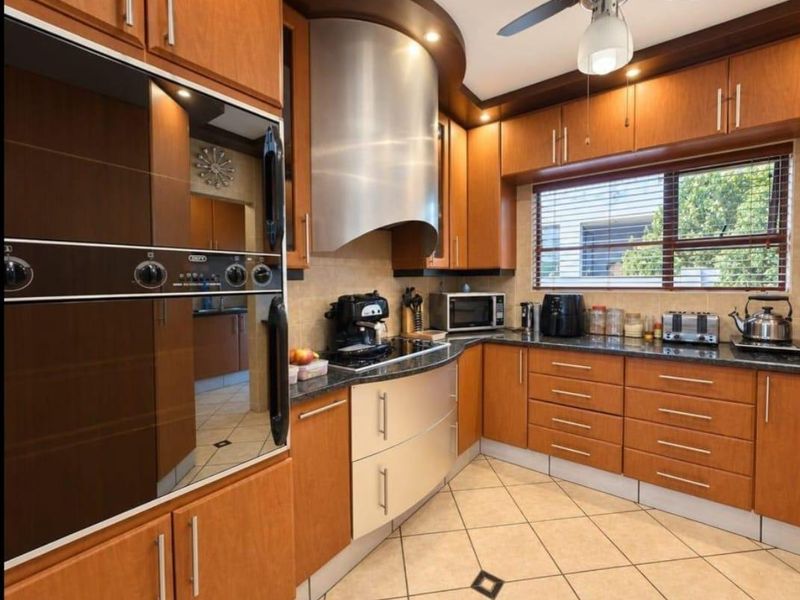 A well-maintained kitchen featuring warm wood cabinetry, granite countertops, a stainless steel extractor fan, and a built-in oven, complemented by tiled flooring.