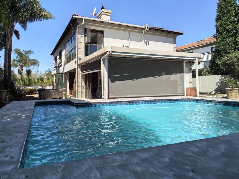 Rear exterior view featuring a swimming pool with tiled coping and a covered patio area equipped with retractable outdoor blinds.