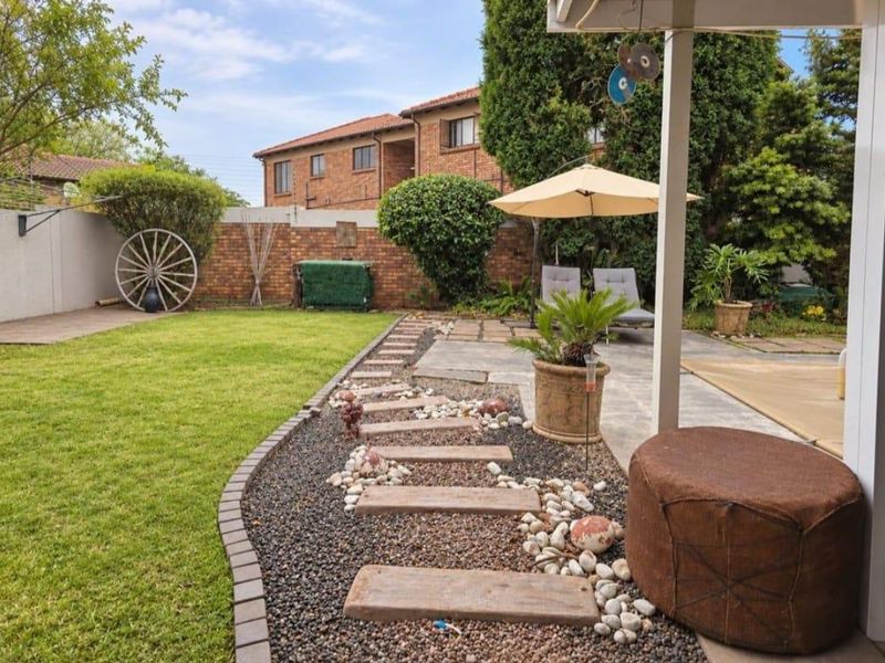 A well-maintained rear garden featuring a paved patio area, lawn, and landscaped gravel pathways enclosed by a brick boundary wall.