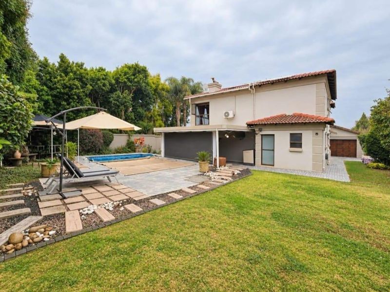Rear view of the property featuring a swimming pool, covered patio area, paved terrace, and a well-maintained garden with boundary walls.