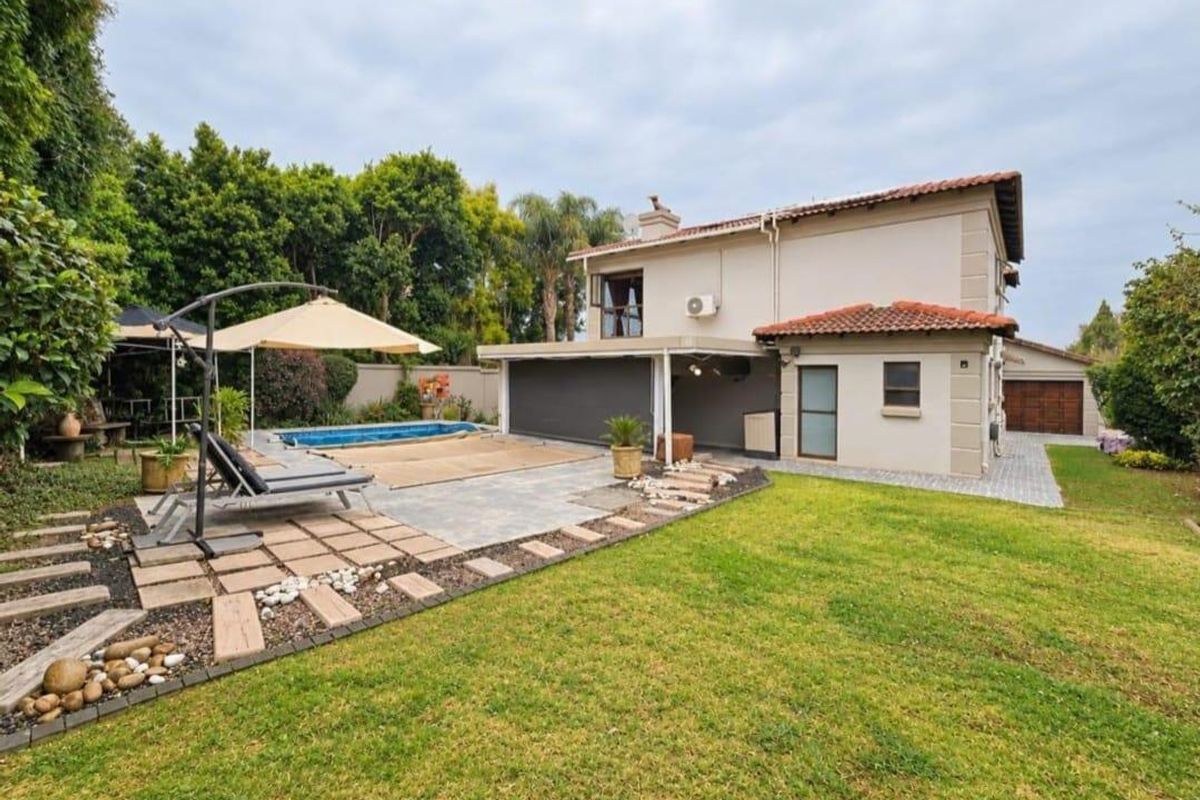 Rear view of the property featuring a swimming pool, covered patio area, paved terrace, and a well-maintained garden with boundary walls.