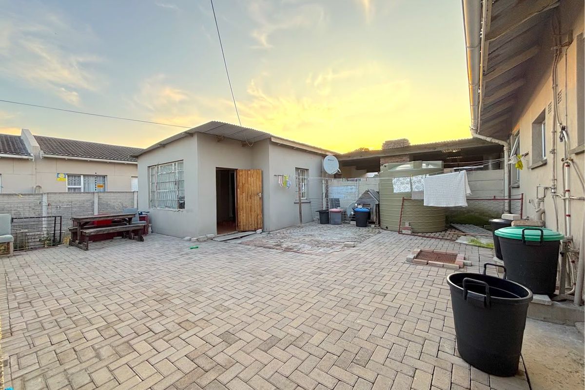 A paved rear courtyard featuring a water storage tank, boundary walls, and access to an outbuilding with a corrugated metal roof.
