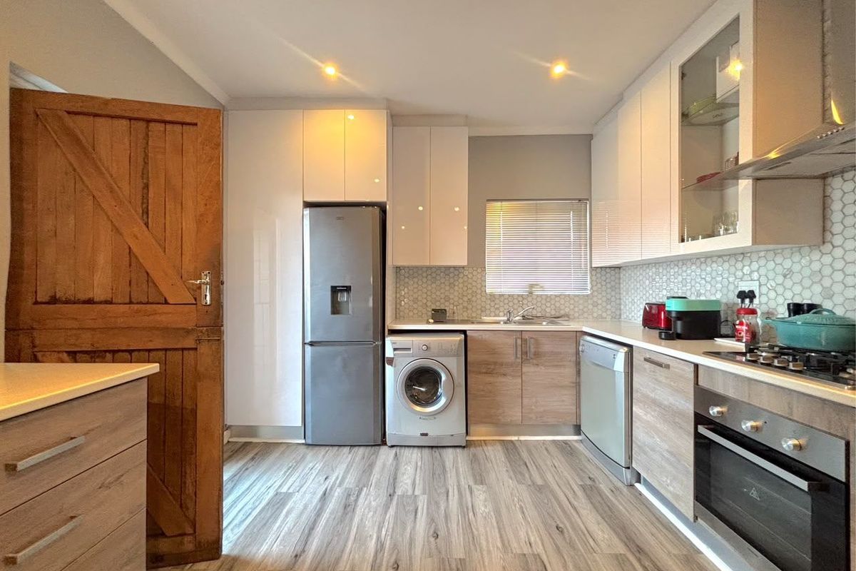 Modern kitchen featuring white and wood-grain cabinetry, mosaic tile backsplash, integrated appliances, and durable laminate flooring with recessed lighting.