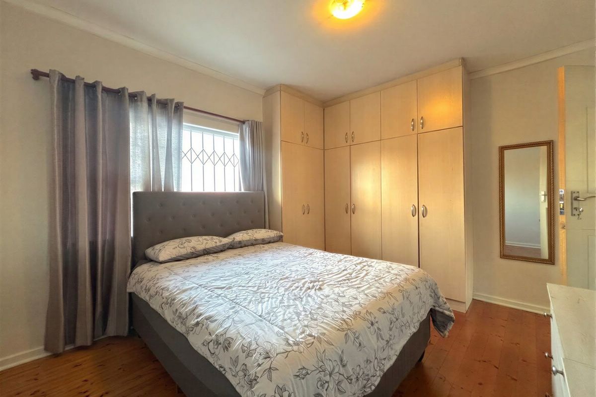 A bedroom featuring timber flooring, built-in corner cupboards, and a window fitted with security bars.