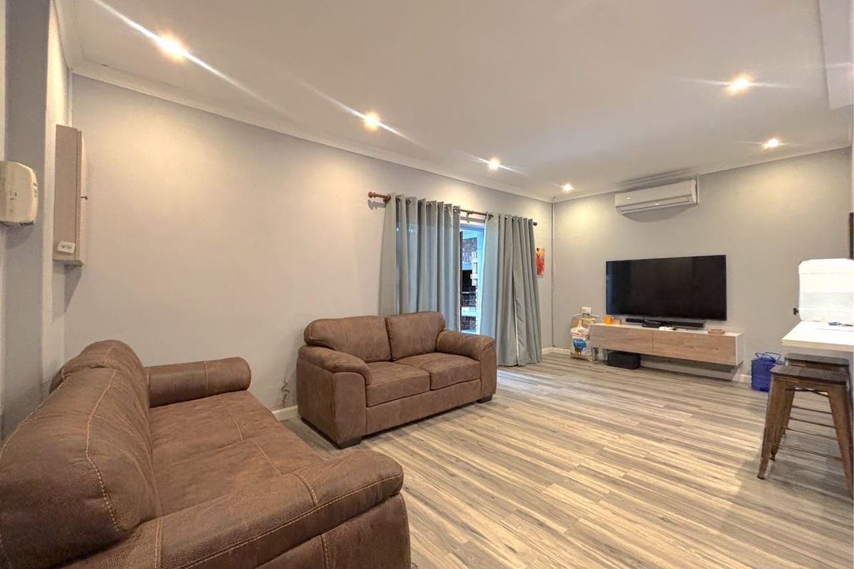 A well-maintained living room featuring modern laminate flooring, recessed downlighting, and a wall-mounted split-system air conditioner.