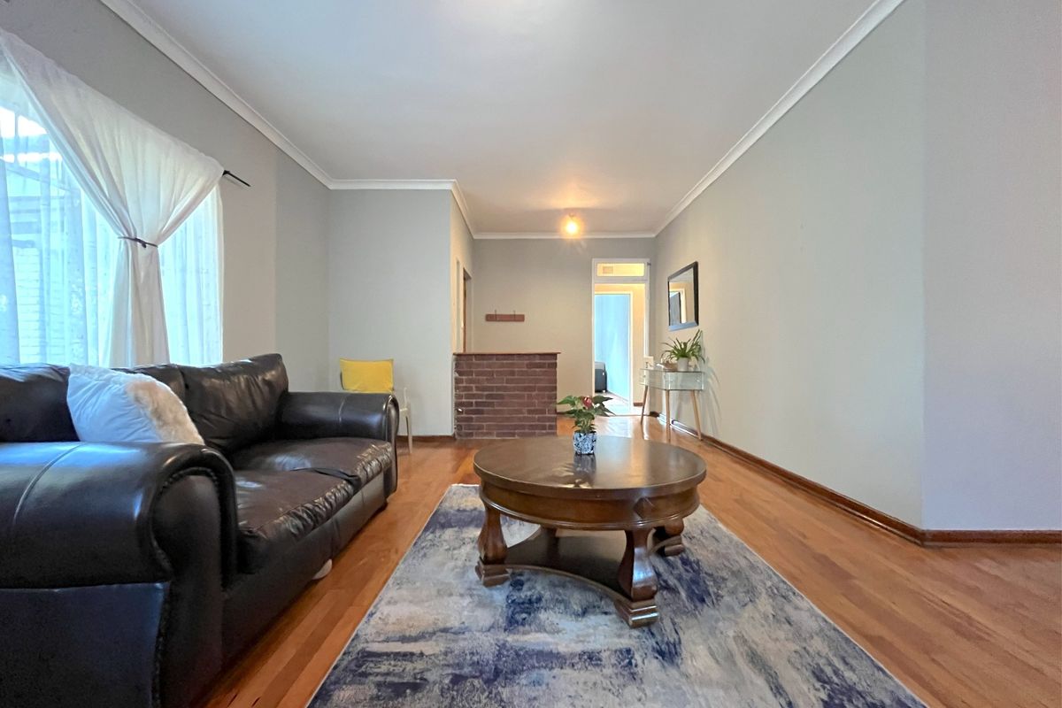 Spacious living room featuring polished hardwood flooring, neutral wall tones, and a distinctive brick partition wall leading to the hallway.
