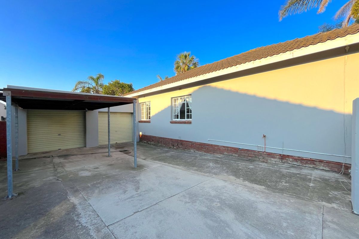 Rear exterior view of the property featuring a concrete driveway, a covered carport, and access to the garage area.