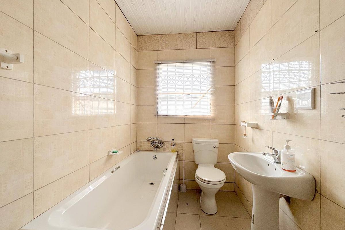 A compact bathroom featuring a standard bathtub, pedestal basin, and toilet, finished with full-height wall tiling and a tiled floor.