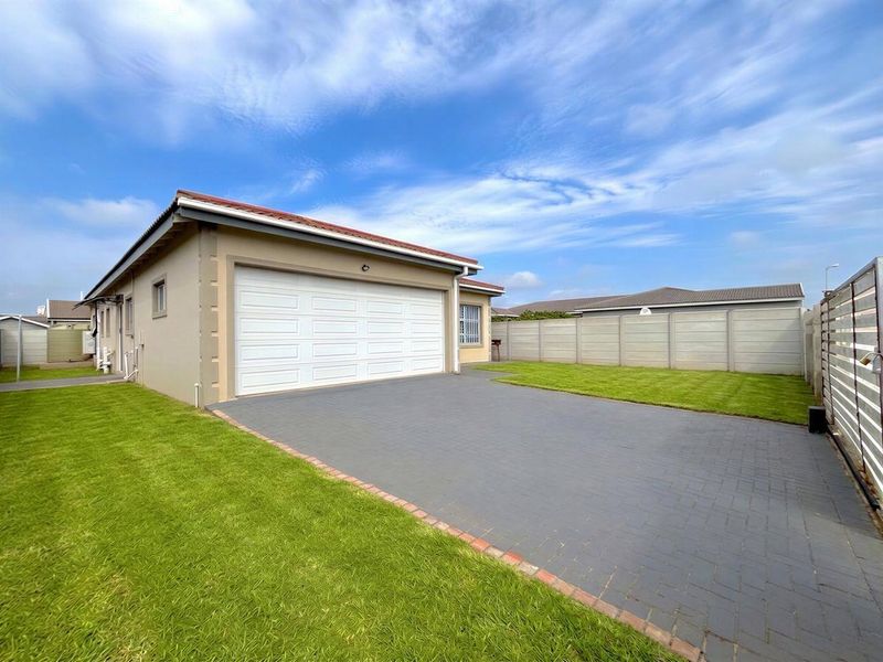 A well-maintained exterior view of the property featuring a paved driveway, double garage, and neat lawn enclosed by precast boundary walls.