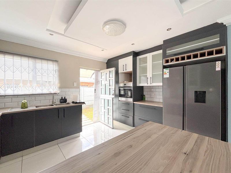 Modern kitchen featuring dark cabinetry, subway tile backsplash, built-in oven, and tiled flooring with direct access to the exterior.